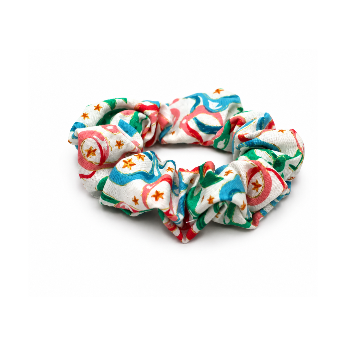 Colorful fabric hair scrunchie with pink, blue, and green abstract shapes and small gold stars on a white background.